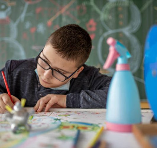 One boy only sitting in classroom and drawing with color pencil Covid-19 inspired theme and social distancing meanning.